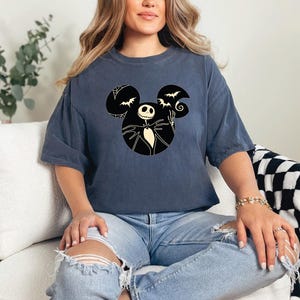 May include: A dark blue t-shirt with a black and white graphic of Jack Skellington from The Nightmare Before Christmas in a Mickey Mouse silhouette. The graphic includes bats and a swirl.