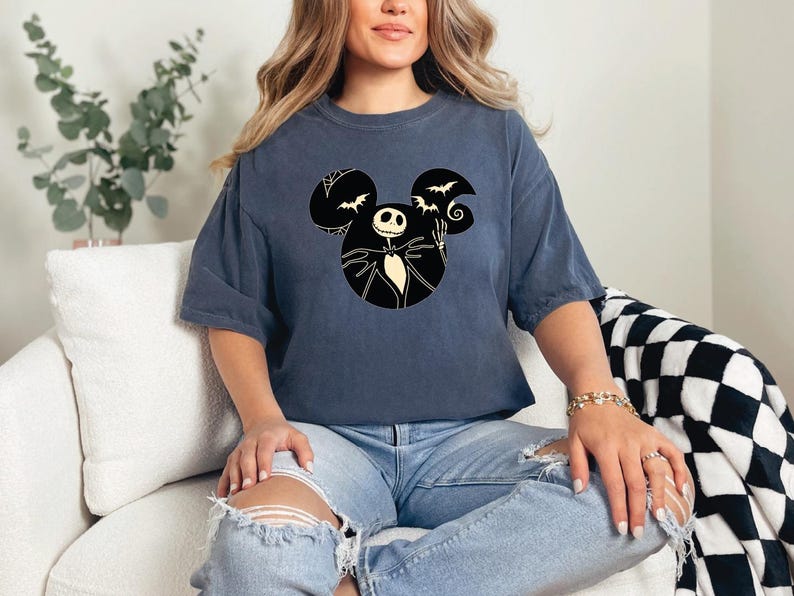 May include: A dark blue t-shirt with a black and white graphic of Jack Skellington from The Nightmare Before Christmas in a Mickey Mouse silhouette. The graphic includes bats and a swirl.