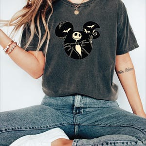 May include: A dark gray t-shirt with a black and white graphic of Jack Skellington from The Nightmare Before Christmas in a Mickey Mouse silhouette. The graphic includes bats and a swirl.