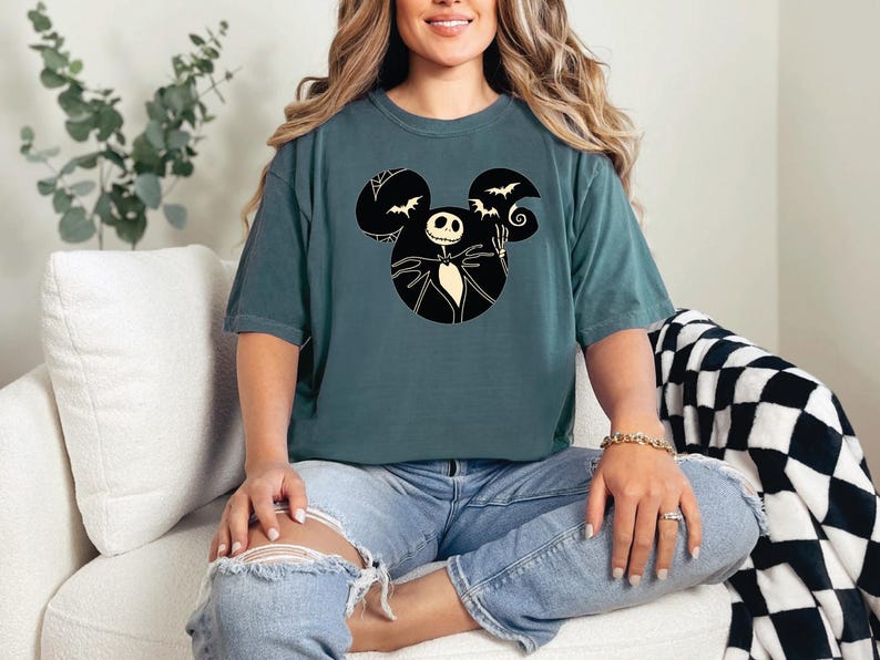 May include: A teal blue t-shirt with a black and white graphic of Jack Skellington from The Nightmare Before Christmas in a Mickey Mouse silhouette. The graphic includes bats and a crescent moon.