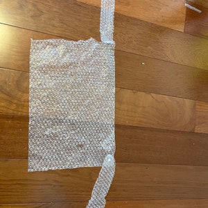 May include: A sheet of bubble wrap with two strips cut out. The strips are attached to the sheet with tape.