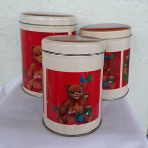 May include: Set of three white ceramic canisters with red and white lids. Each canister features a different illustration of a teddy bear with Christmas-themed decorations. The canisters are perfect for storing sugar, flour, or other kitchen staples.