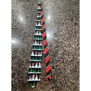 May include: A black necktie featuring a repeating horizontal pattern of snowmen and green Christmas trees. The narrow end of the tie displays a diagonal stripe pattern in red, green, and black, decorated with small gold-colored bell illustrations.