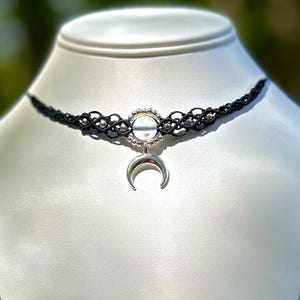 May include: A black choker necklace with a silver crescent moon charm and a circle pendant with clear rhinestones.