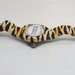 May include: A black and orange zebra-print wristwatch with a white face that reads "STAR.T 2000 NEW YORK".