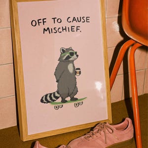 Puede incluir: Un cuadro enmarcado con el texto "OFF TO CAUSE MISCHIEF" muestra un mapache con gafas de sol y una taza de caf&eacute; en un monopat&iacute;n. Zapatillas rosas con suelas marrones en primer plano. El marco es de madera.