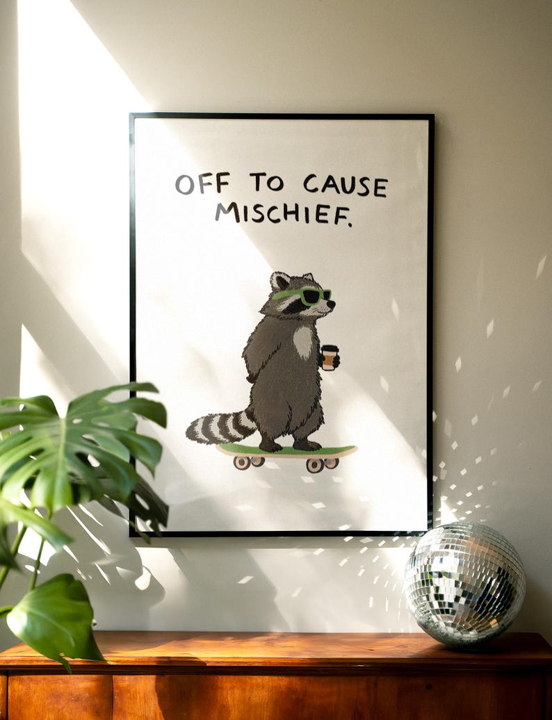 Puede incluir: Una impresi&oacute;n art&iacute;stica enmarcada con un mapache de dibujos animados en monopat&iacute;n, con gafas de sol y una taza de caf&eacute;. La impresi&oacute;n tiene el texto "OFF TO CAUSE MISCHIEF". El mapache es gris y blanco, sobre un fondo blanco.