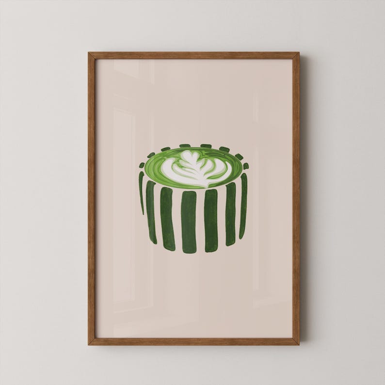 May include: A framed art print featuring a green matcha latte with latte art. The drink is in a striped cup, with a light beige background. The frame is a warm brown color.