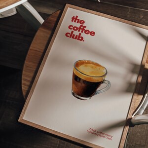 Puede incluir: Un p&oacute;ster enmarcado con una ilustraci&oacute;n de acuarela de una taza de caf&eacute;. El p&oacute;ster tiene el texto "the coffee club." y "fresh coffee every morning from 7am" en rojo.