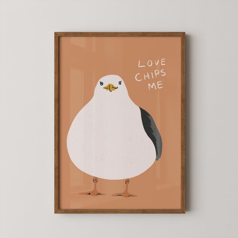 May include: A framed wall art print featuring a stylized illustration of a round white seagull with a dark gray wing and orange feet against a solid terracotta background. The text LOVE CHIPS ME is printed in white in the upper right corner.