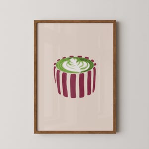 May include: A framed art print featuring a stylized illustration of a matcha latte. The drink is in a cylindrical cup with vertical burgundy stripes. The matcha is topped with a white latte art design, set against a light beige background.