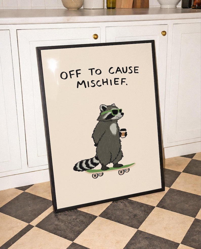Puede incluir: L&aacute;mina enmarcada con un mapache con gafas de sol y una taza de caf&eacute; sobre una patineta. La impresi&oacute;n tiene el texto "OFF TO CAUSE MISCHIEF" en negro sobre un fondo crema. El marco es negro.