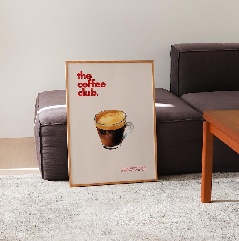 Puede incluir: Un p&oacute;ster enmarcado con el texto "the coffee club." en letras rojas. El p&oacute;ster presenta una ilustraci&oacute;n de acuarela de una taza de caf&eacute; sobre un fondo marr&oacute;n.