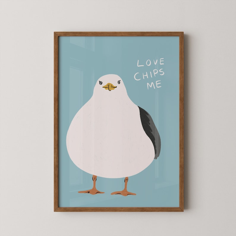 May include: A framed wall art print featuring a stylized illustration of a round white seagull with a dark gray wing and orange feet against a light blue background. The text LOVE CHIPS ME is written in white letters in the upper right corner.