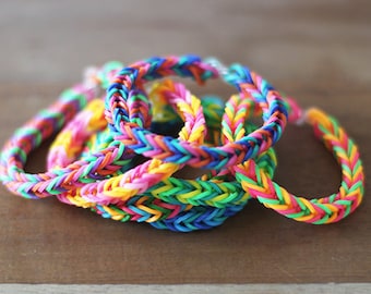 May include: A stack of colorful rainbow loom bracelets made with rubber bands. The bracelets are in a variety of colors, including pink, blue, green, yellow, and orange.