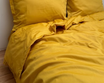 May include: A mustard yellow duvet cover and two matching pillowcases. The bedding is made of a soft, smooth fabric and has a subtle sheen.