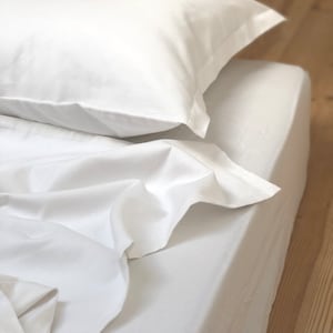 May include: A white bed with a white pillow on top. The sheets are smooth and wrinkle-free.