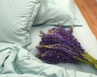 May include: A light blue bedding set with a bouquet of purple lupine flowers on top.