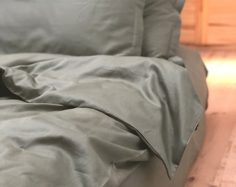 Könnte beinhalten: Ein Bett mit einem Bettkastenbezug und Kissenbezügen in Salbeigrün. Die Bettwäsche ist glatt und faltenfrei und sorgt für ein luxuriöses und einladendes Ambiente.