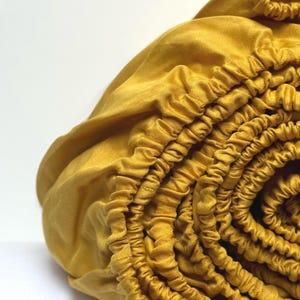 May include: A close-up of a mustard yellow fitted sheet rolled up. The sheet has a stretchy elastic band around the edge.