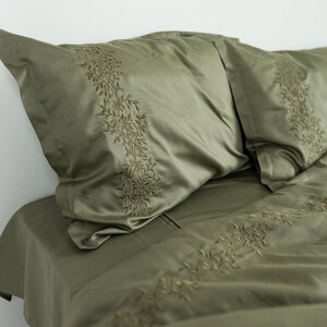 May include: A green bedding set with embroidered leaf designs. The set includes a duvet cover and two pillowcases.