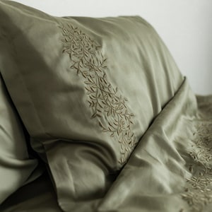 May include: A green pillowcase with a delicate embroidered floral design. The pillowcase is made of a soft, smooth fabric.