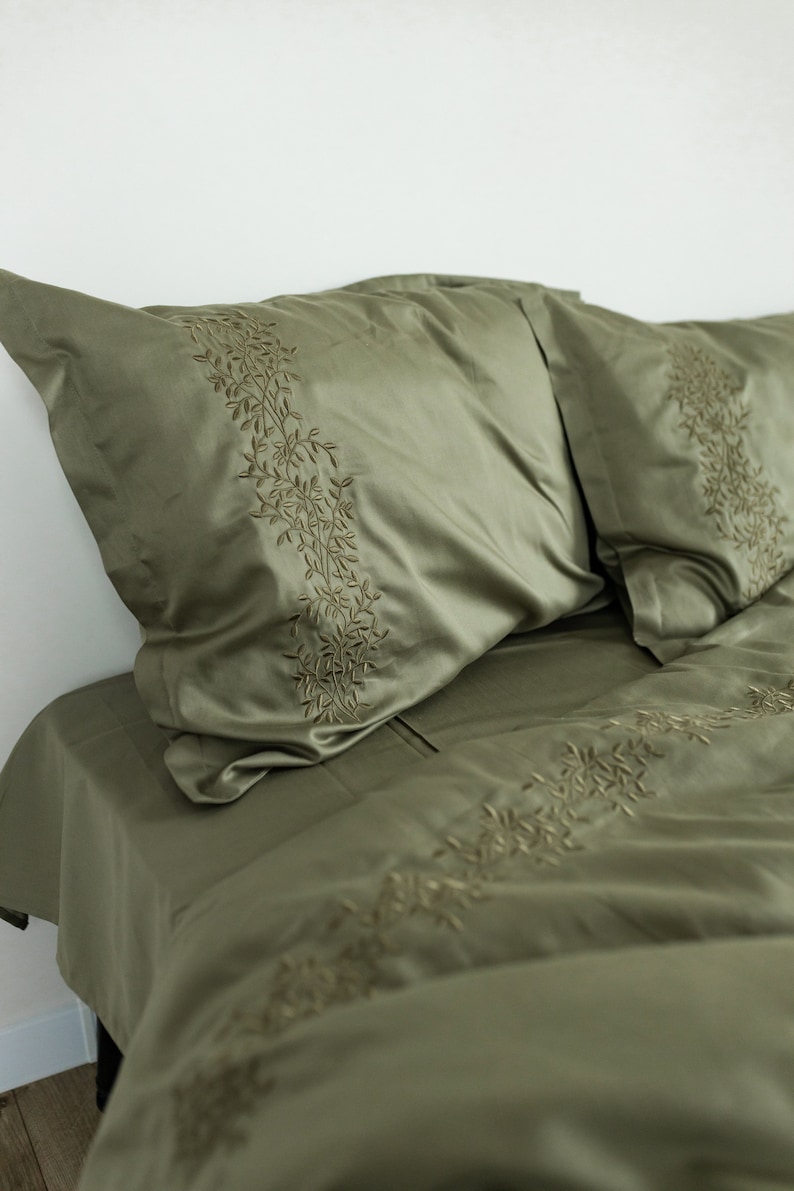 May include: A green bedding set with embroidered leaf designs. The set includes a duvet cover and two pillowcases.