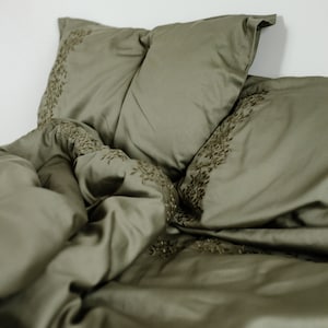 May include: A green duvet cover and two matching pillowcases with an embroidered floral design.