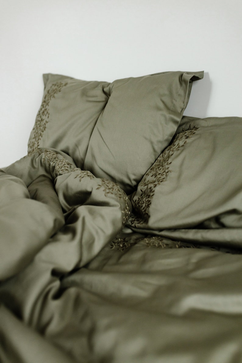 May include: A green duvet cover and two matching pillowcases with an embroidered floral design.