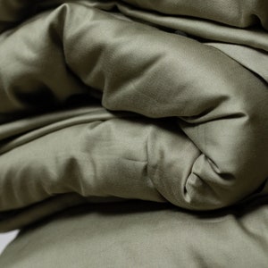May include: Close-up of a soft, green fabric folded in layers. The fabric has a smooth, silky texture.