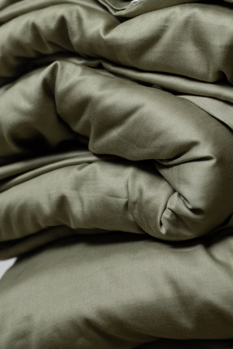 May include: Close-up of a soft, green fabric folded in layers. The fabric has a smooth, silky texture.