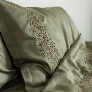 May include: A green pillowcase with a delicate embroidered floral design. The pillowcase is made of a soft, smooth fabric.