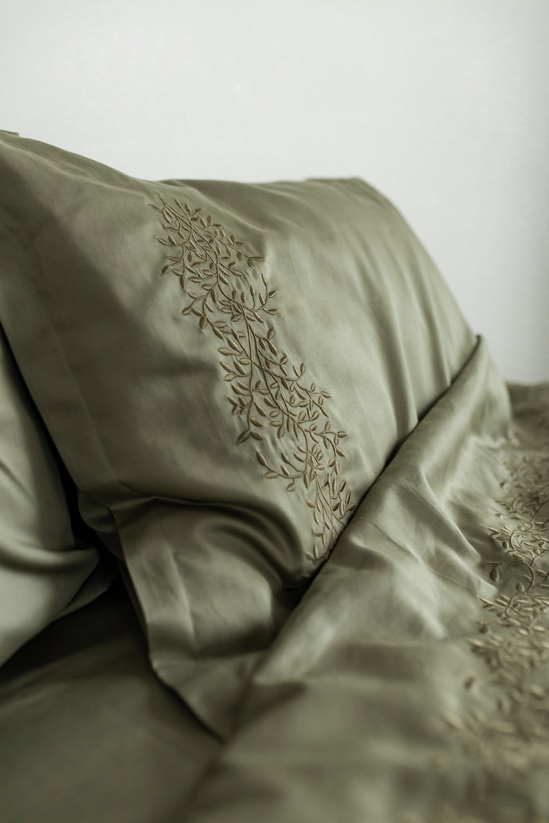 May include: A green pillowcase with a delicate embroidered floral design. The pillowcase is made of a soft, smooth fabric.