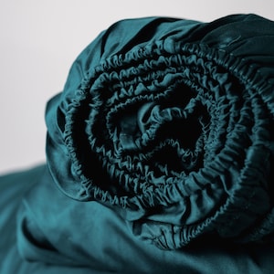 Può includere: Un lenzuolo con angoli elasticizzato blu turchese arrotolato in un rotolo stretto, mostrando il bordo elastico. Il lenzuolo è fatto di un tessuto morbido e liscio.