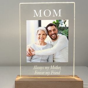 May include: A clear acrylic photo frame with a wooden base. The frame has a photo of a woman and a man hugging. The text "MOM" is at the top of the frame and the text "Always my Mother, Forever my Friend" is at the bottom.