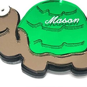 Könnte beinhalten: Ein grüner Schildkröten-Schlüsselanhänger mit brauner Schale und weißem Gesicht. Auf der Schale der Schildkröte steht der Name "Mason" in weiß.