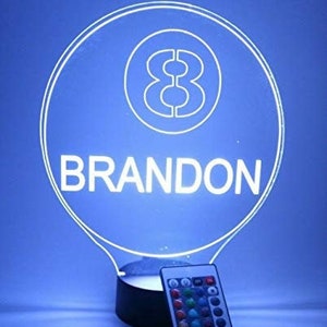 May include: A white LED night light shaped like a light bulb with a white 8-ball design and the name "BRANDON" printed below. The light is on a black base and comes with a remote control.
