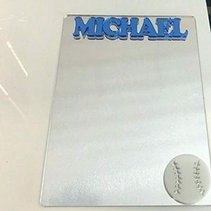May include: A blue acrylic mirror with the name "MICHAEL" in blue letters at the top. A white baseball with black stitching is at the bottom right corner.