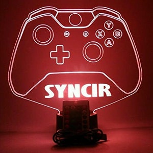 以下が含まれることがあります： 「SYNCIR」という文字の下に、ビデオゲームコントローラーの白いアウトラインがあります。コントローラーは赤く光っており、ベースにリモコンが付いています。