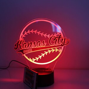 May include: A baseball-themed LED lamp with the words "Kansas City" in red script, and "STEVE" below. The lamp is illuminated with a red glow, and has a remote control.