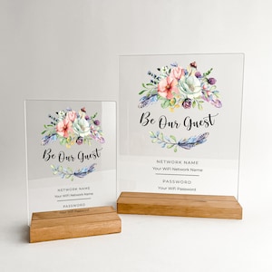 May include: Two clear acrylic signs with a floral design and the text "Be Our Guest". The signs have a wooden base and include spaces for the WiFi network name and password.