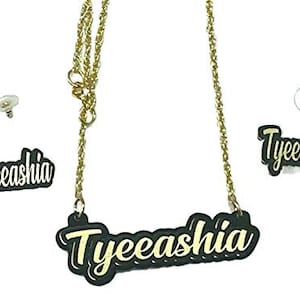 Könnte beinhalten: Goldkette mit einem schwarzen Namensschild-Anhänger, auf dem "Tyeeashia" steht. Das Set enthält außerdem ein Paar passende Ohrringe mit schwarzen Namensschildern, auf denen "Tyeeashia" steht.