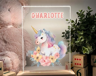 May include: A clear acrylic night light with a wooden base. The light features a colorful unicorn illustration with flowers and the name "CHARLOTTE" in pink lettering.