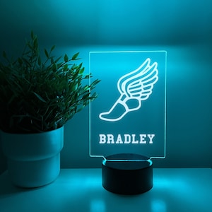 May include: A blue LED night light with a white silhouette of a winged running shoe and the name "BRADLEY" printed below.