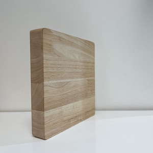 May include: A light brown wooden cutting board with a smooth surface. The board is made of multiple pieces of wood that have been joined together.