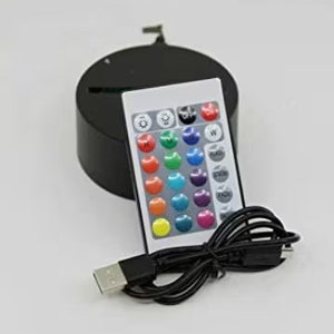 May include: A black LED light base with a remote control and USB cable. The remote has multiple color options and control buttons. The base is round and has a slot for an item to be displayed.