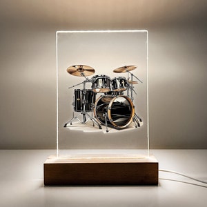 May include: A black drum set with a bass drum, two toms, and a snare drum. The drums are set up on a stand with cymbals and a hi-hat. The drum set is illuminated by a light source above.