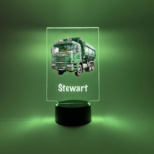 May include: A green toy truck with a white cab and the name "Stewart" printed on the base of a clear acrylic night light.