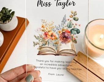 May include: A clear acrylic plaque with a floral design and an open book. The text "Miss Taylor" is at the top of the plaque. The text "Thank you for making learning an incredible adventure! I'm grateful to have you as my teacher. From Laurel" is at the bottom of the plaque.