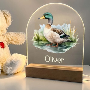 May include: A wooden base with a clear acrylic panel featuring a watercolor illustration of a mallard duck. The panel is illuminated from behind and the name "Oliver" is printed below the duck.